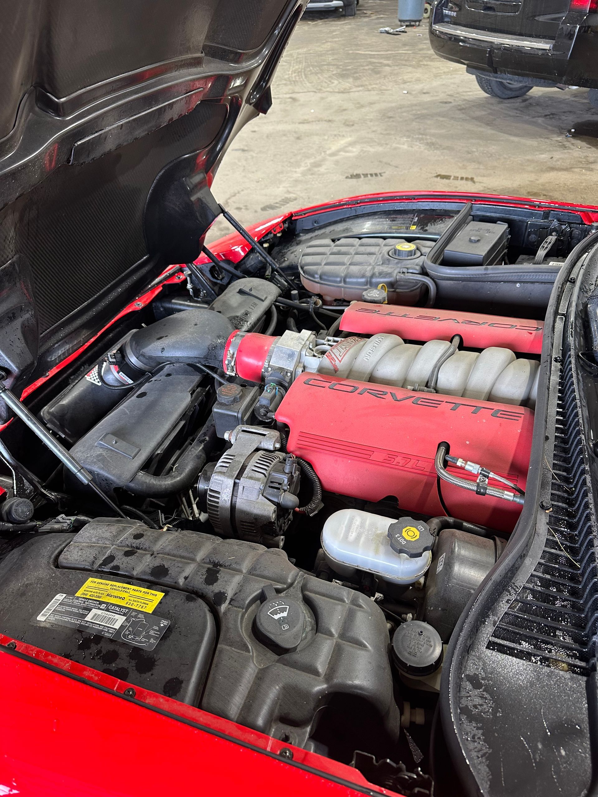 Open car hood showing a red engine bay with black components in a garage