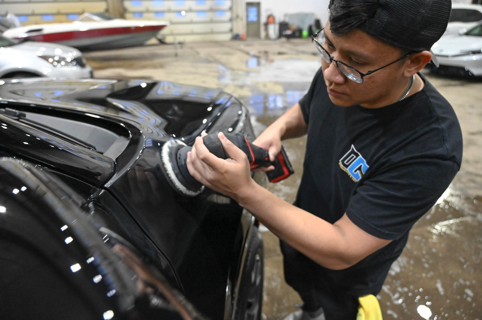 Person polishing a black car with a buffer in a workshop