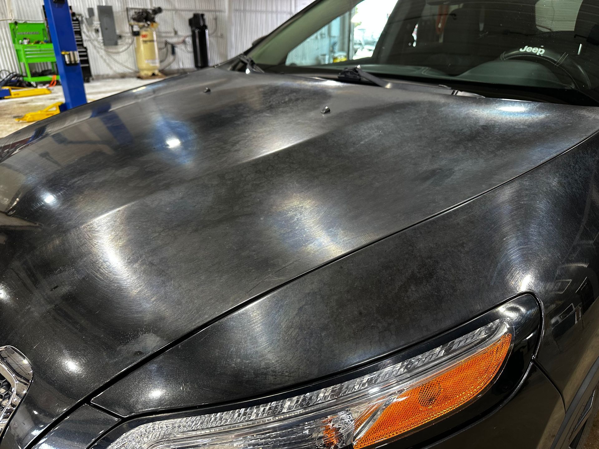 Black car hood with water droplets in a garage, close-up of front headlight and windshield corner