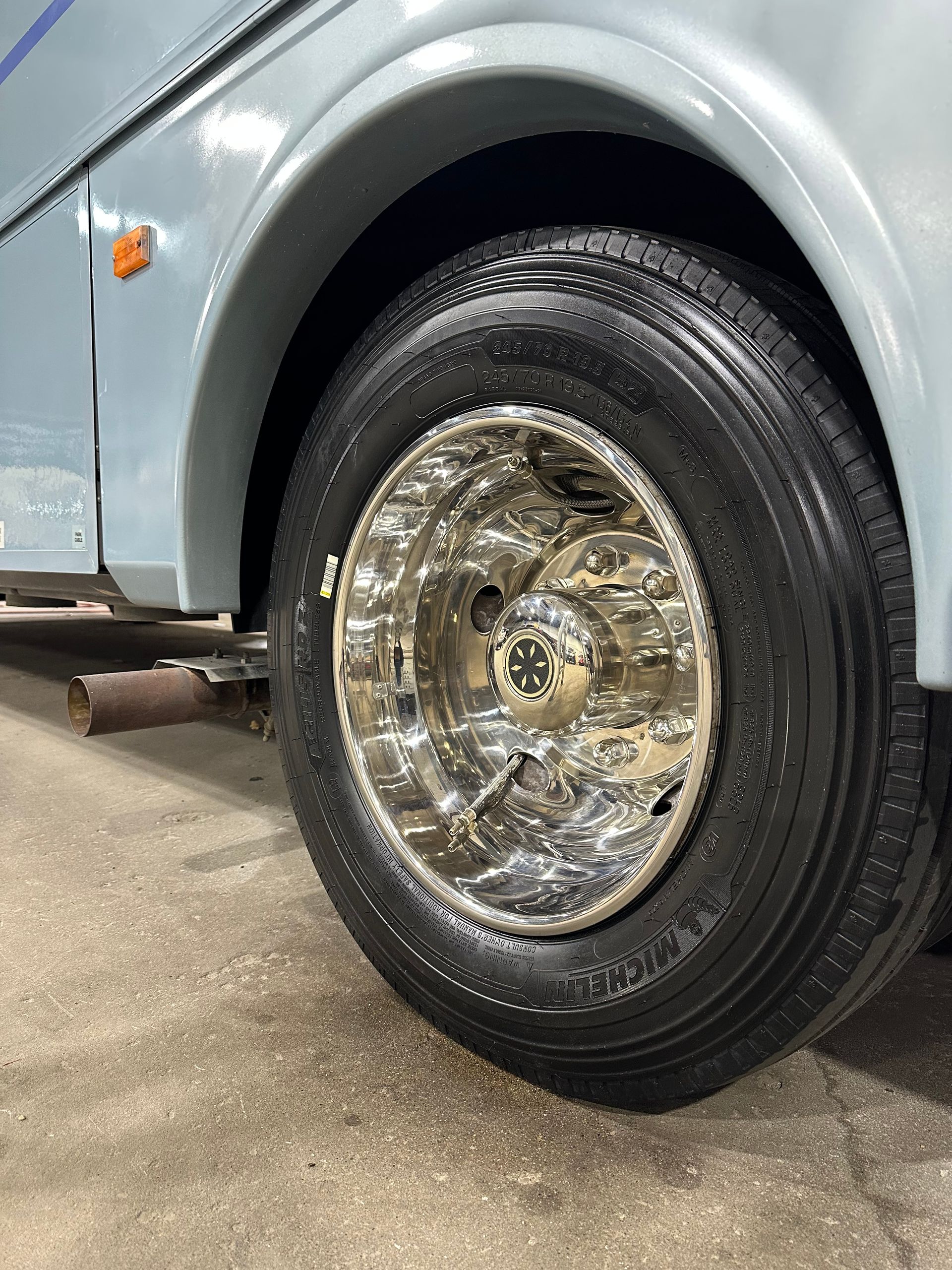Close-up of a vintage car’s shiny chrome wheel and black tire on a light blue vehicle.