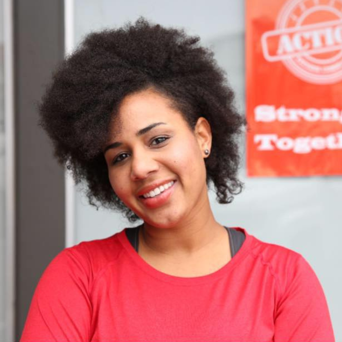 A woman in a red shirt is smiling in front of a sign that says strong together