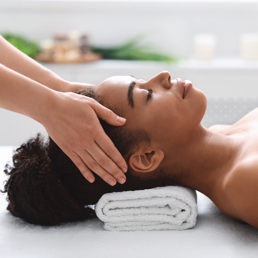 A woman is laying on a table getting a head massage