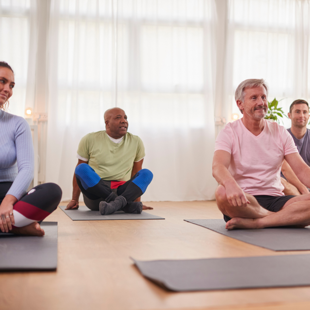 A group of people are sitting on yoga mats in a room.