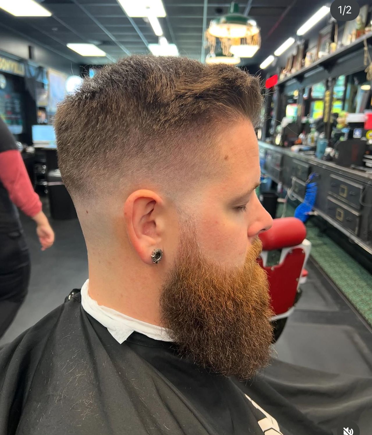 Man with a fade haircut and beard sitting in a barbershop chair, side profile