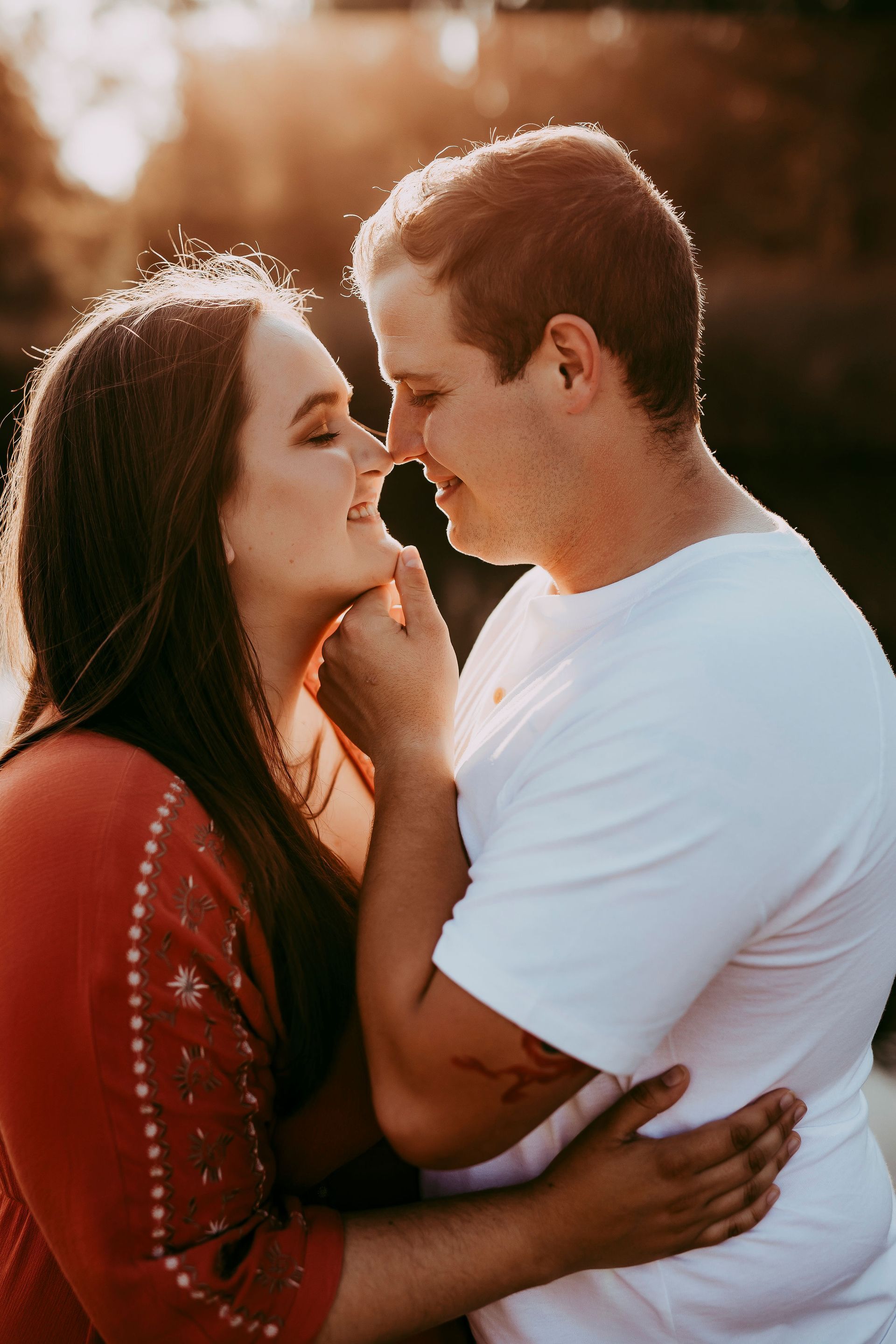 Couple in embrace, smiling. Woman touches man's face. Golden sunlight.