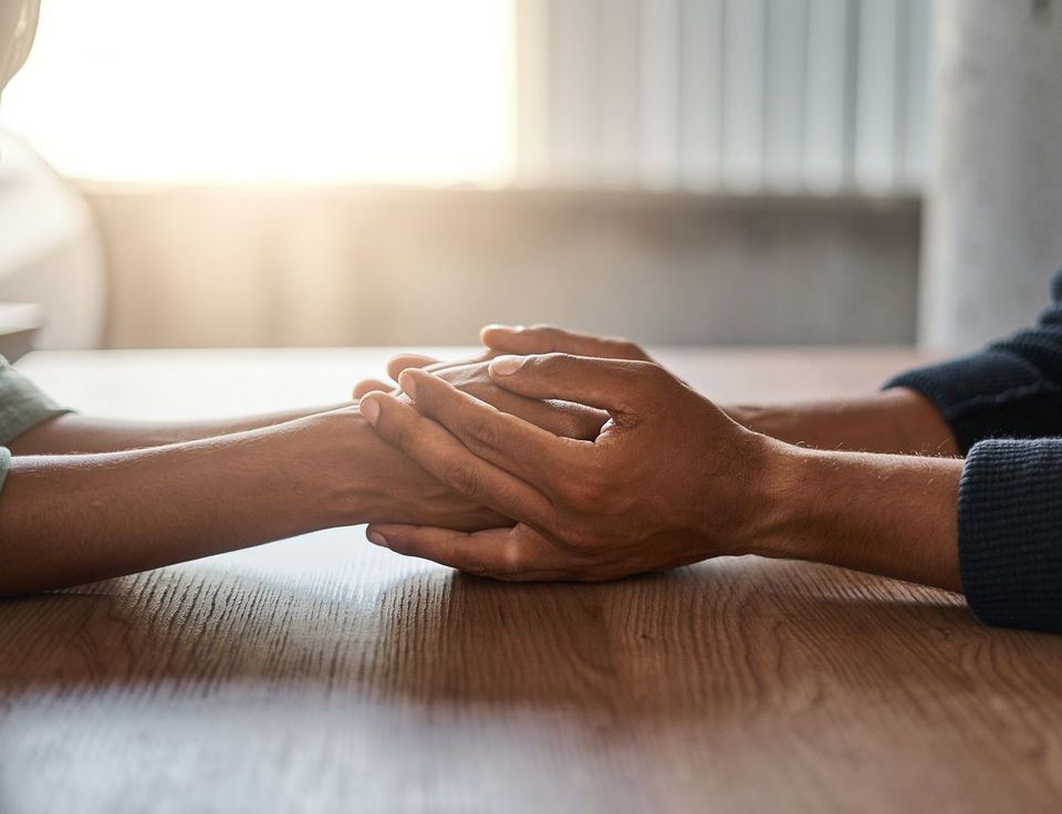 Two people holding hands across a table, offering comfort and emotional support during a difficult time.