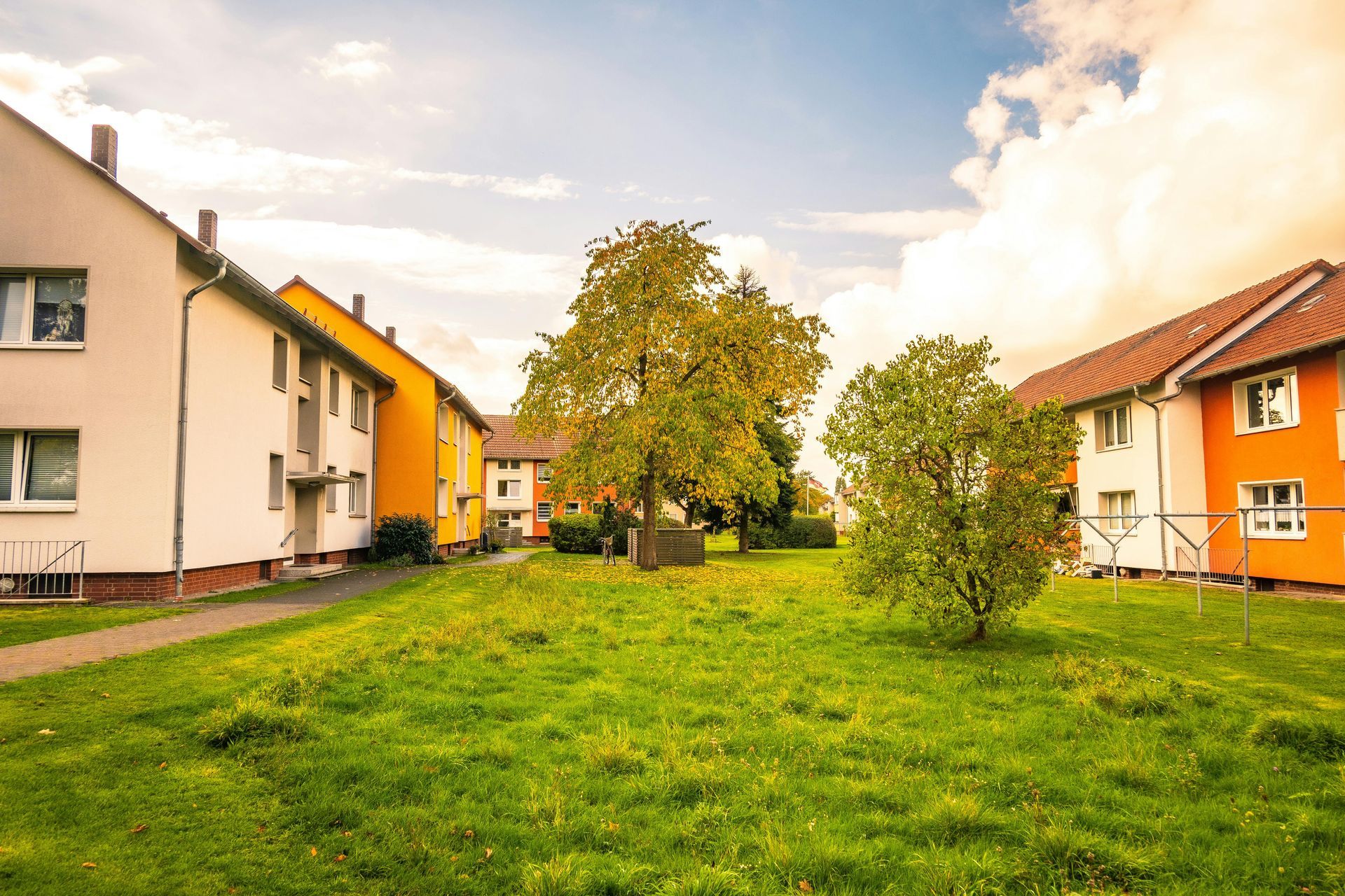 A grassy courtyard between two rows of two-story residential buildings painted in white and orange under a bright sky.