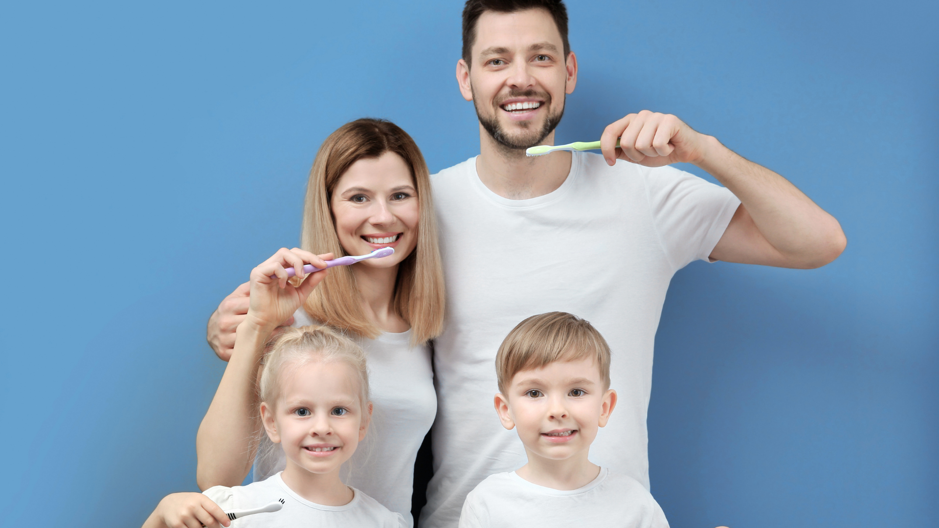 Family of four brushing teeth together, smiling against a blue background.