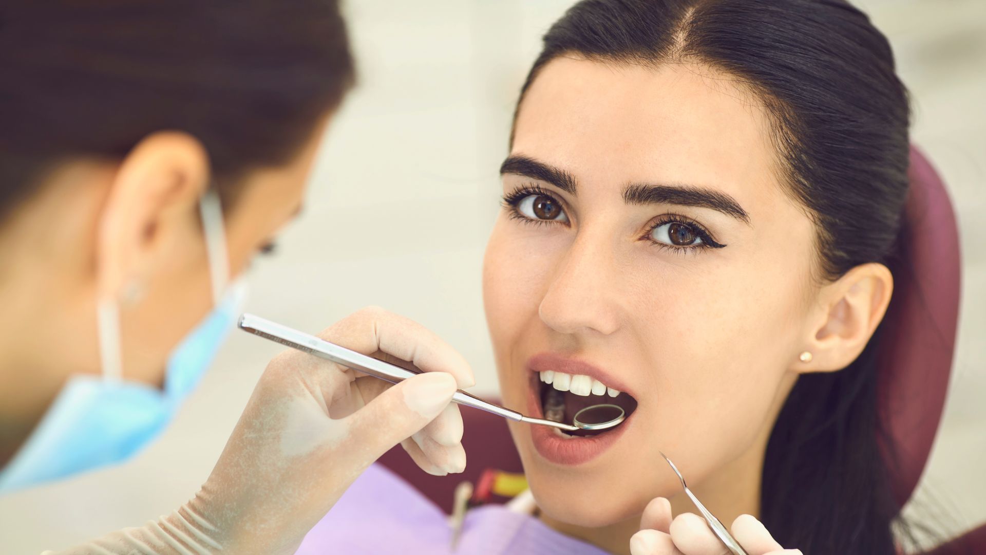 Dentist examining a patient’s open mouth with dental tools in a clinic