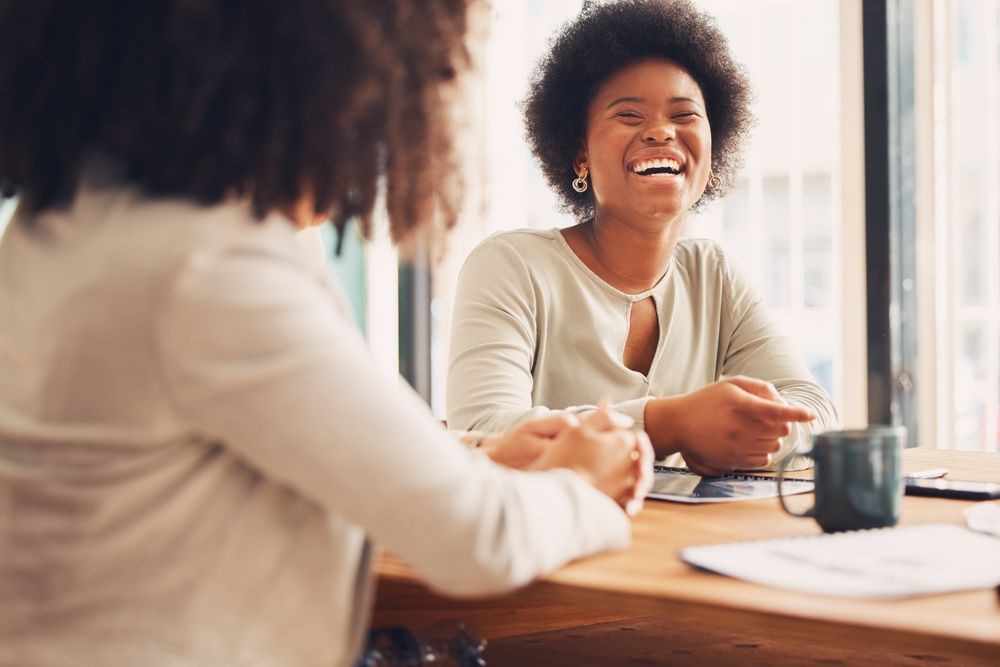 Two women are sitting at a table having a conversation and laughing.