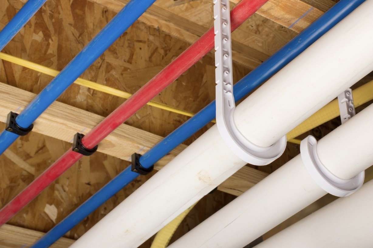 Pipes secured to wooden beams with clips; red, blue, and white pipes are visible.