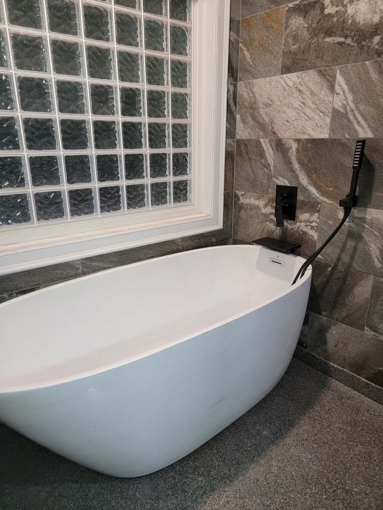 White bathtub filled with water beside a stone wall and glass block window. Black showerhead on the right.
