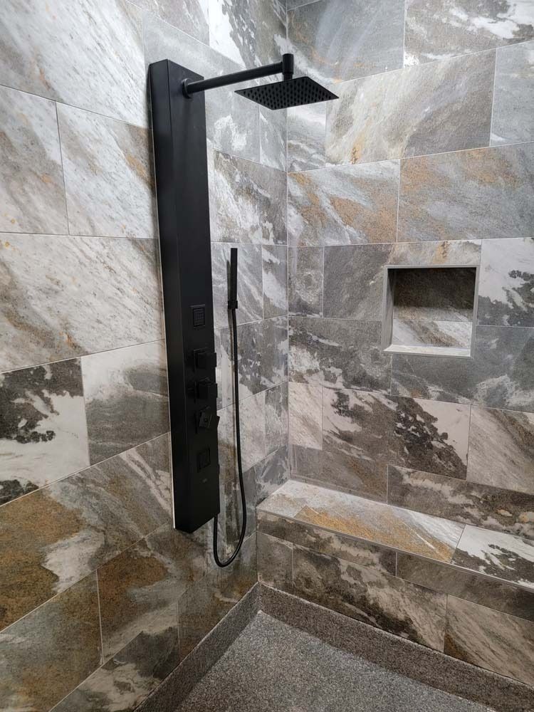 Black shower panel with rain shower head, hand shower, and tiled walls in a modern bathroom.