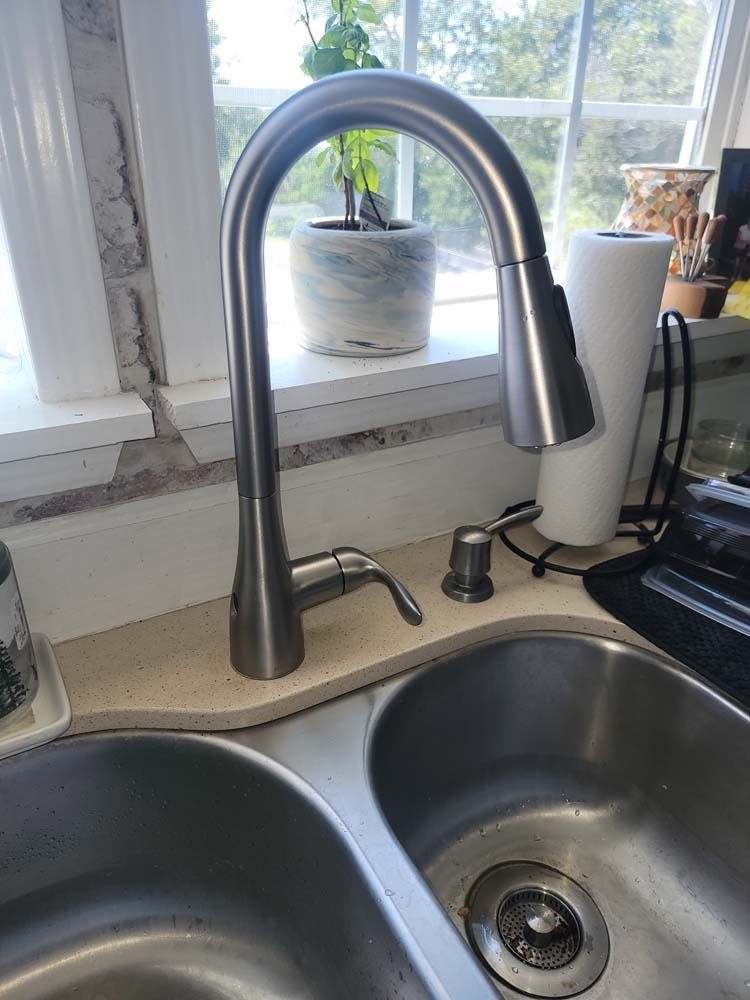 Stainless steel kitchen faucet over a double sink, beside a soap dispenser. A window is in the background.