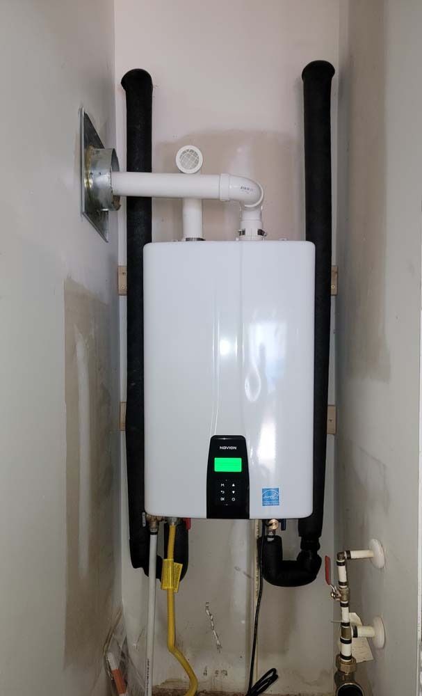 White tankless water heater installed on a wall with black insulated pipes and vent.