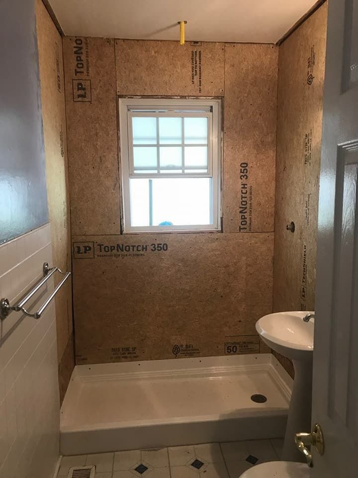Bathroom undergoing renovation, featuring a shower base, sink, window, and exposed wall paneling.