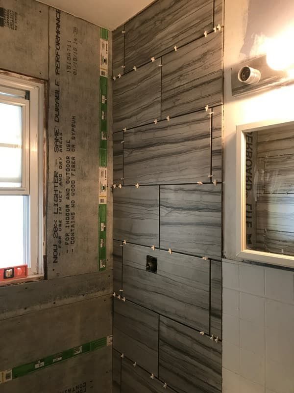 Shower tile installation in progress; gray and white textured tiles with green spacers.