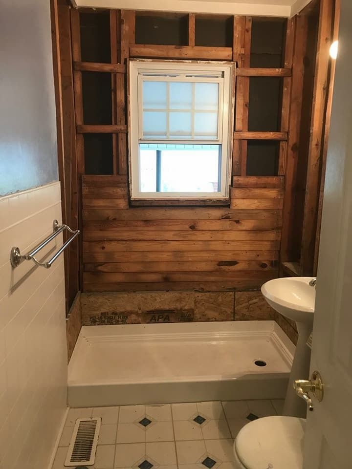 Bathroom under renovation with exposed wood framing, white fixtures, and patterned flooring.