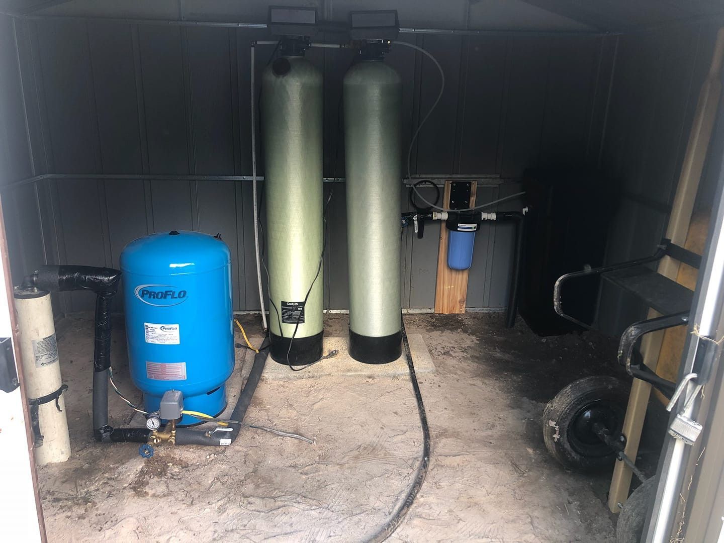 Water filtration system with pressure tank and two tall tanks inside a shed.