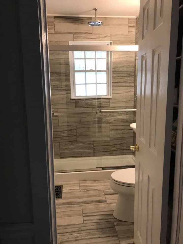 Bathroom with gray tiled shower and floor, toilet, window, glass shower door.