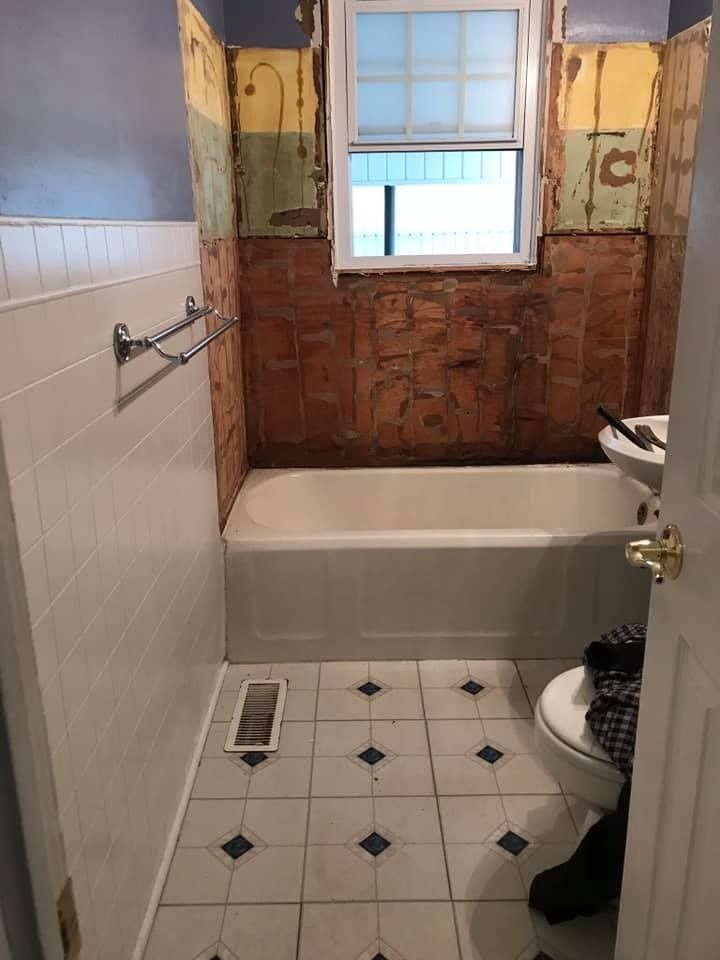 Bathroom under renovation, with exposed wall behind the tub, white tile, and a patterned floor.