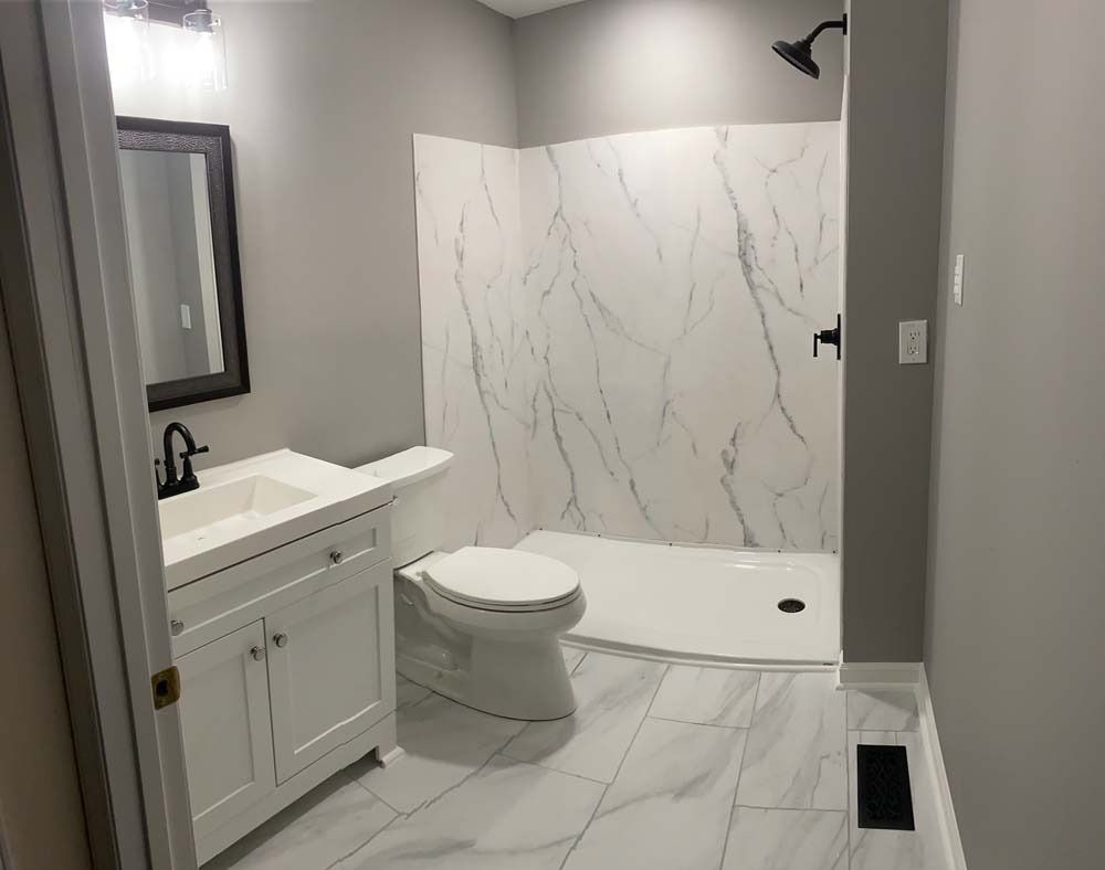 Bathroom with white vanity, marble shower, toilet, and gray walls.