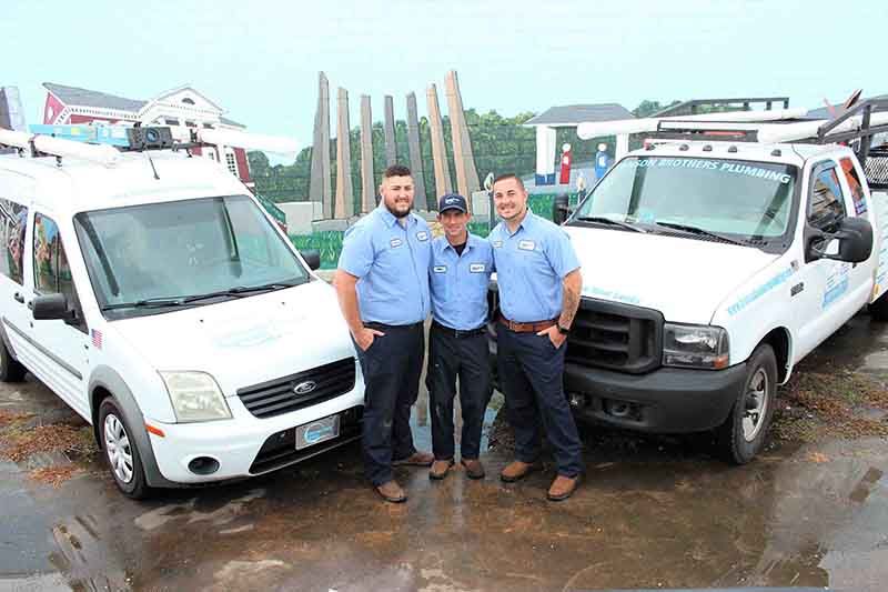 Three men in uniform stand between two white work trucks.