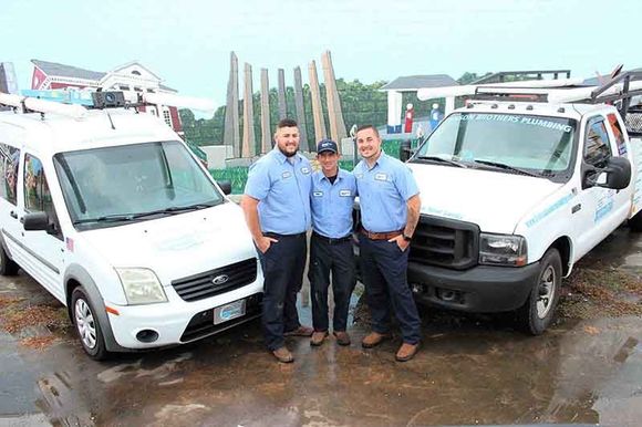 Three men in uniform stand between two white work trucks.