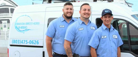 Three men in blue shirts stand in front of a white van with the words 