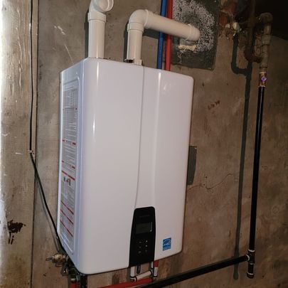 White tankless water heater installed on a concrete wall with connected pipes.