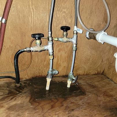 Plumbing pipes and shutoff valves under a sink on a wood surface.