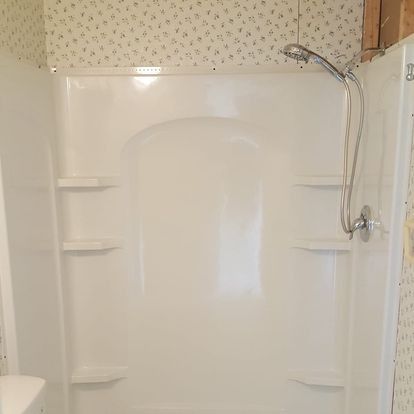 White, one-piece shower unit with built-in shelves. Silver showerhead and faucet. Wallpaper above.