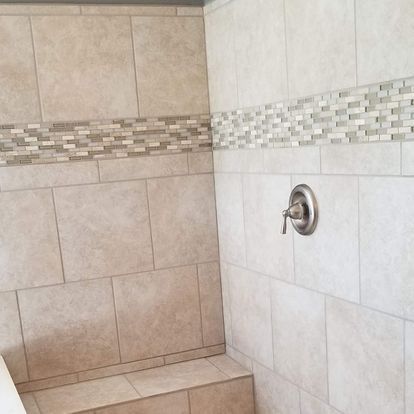 Bathroom shower with beige tile walls, mosaic accent, and silver fixtures.