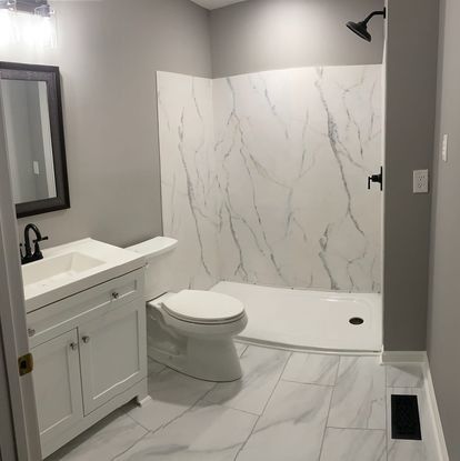 Bathroom with white marble-look shower and floor tiles, white vanity, black fixtures, and gray walls.