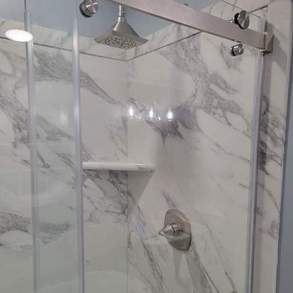 Shower with marble-patterned walls, a glass door, silver hardware, and a built-in shelf.