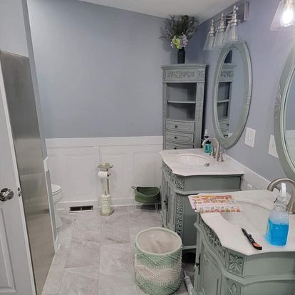Bathroom with blue walls, two sinks, and a tall cabinet. Gray marble floor and white wainscoting.