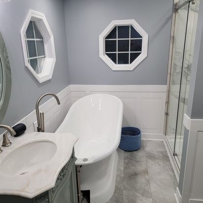 Bathroom with white clawfoot tub, octagonal windows, gray walls, marble vanity, and glass shower.