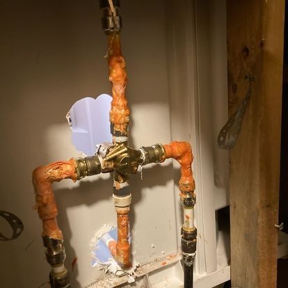 Copper plumbing pipes with orange insulation and brass fittings against a white wall.
