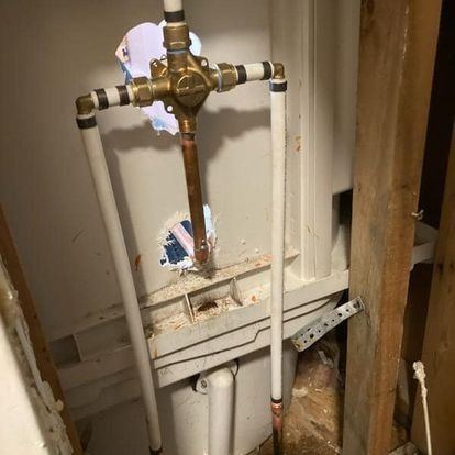 Plumbing fixture with copper and white pipes against a partially demolished wall.