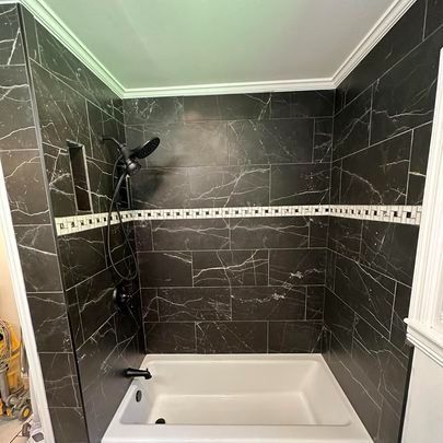 Bathroom with black marble tile shower walls, white tub, and black fixtures.