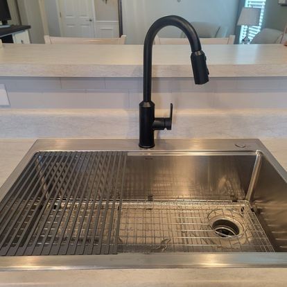 Black faucet over a stainless steel kitchen sink with two metal grids.