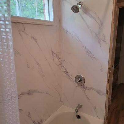 Shower with white marble-patterned walls, chrome fixtures, and a white bathtub. A window is visible.