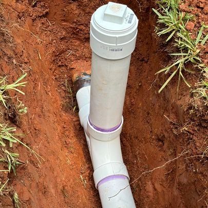 PVC pipes installed in a trench, with a white cap, connecting to an existing pipe.