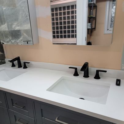 Bathroom vanity with two white sinks, dark faucets, and gray cabinets.