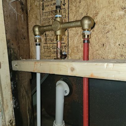 Plumbing fixtures installed in a wall: copper faucet, connected to red and white pipes.