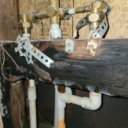 Water pipes and valves attached to a burnt wood beam, with rusted metal straps.