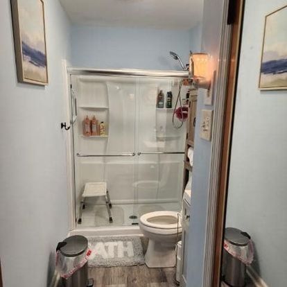 Small bathroom with a shower, toilet, and a step stool. Blue walls.