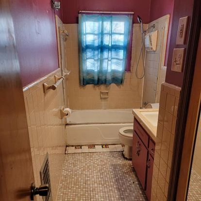 Small bathroom with white tiled walls, a bathtub, toilet, and sink. The walls are painted pink.