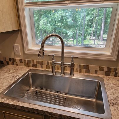 Stainless steel kitchen sink with faucet, window overlooking trees.