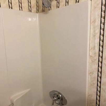 White corner shower with showerhead and faucet against patterned wallpaper.